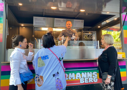 Food-Trailer Der Hermannsberg - Ein Mitarbeiter im Food-Truck überreicht einer Kundin Ihre Bestellung